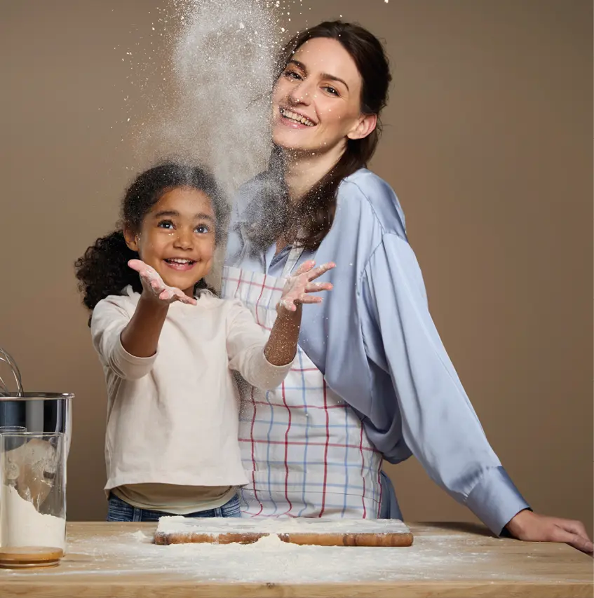 Mutter und Kind backen gemeinsam in der Küche, Mehl wirbelt durch die Luft und sorgt für spielerische Momente. Die Szene steht für Familienleben, Freude am Kochen und eine moderne wohnliche Küche mit Wohlfühlatmosphäre.